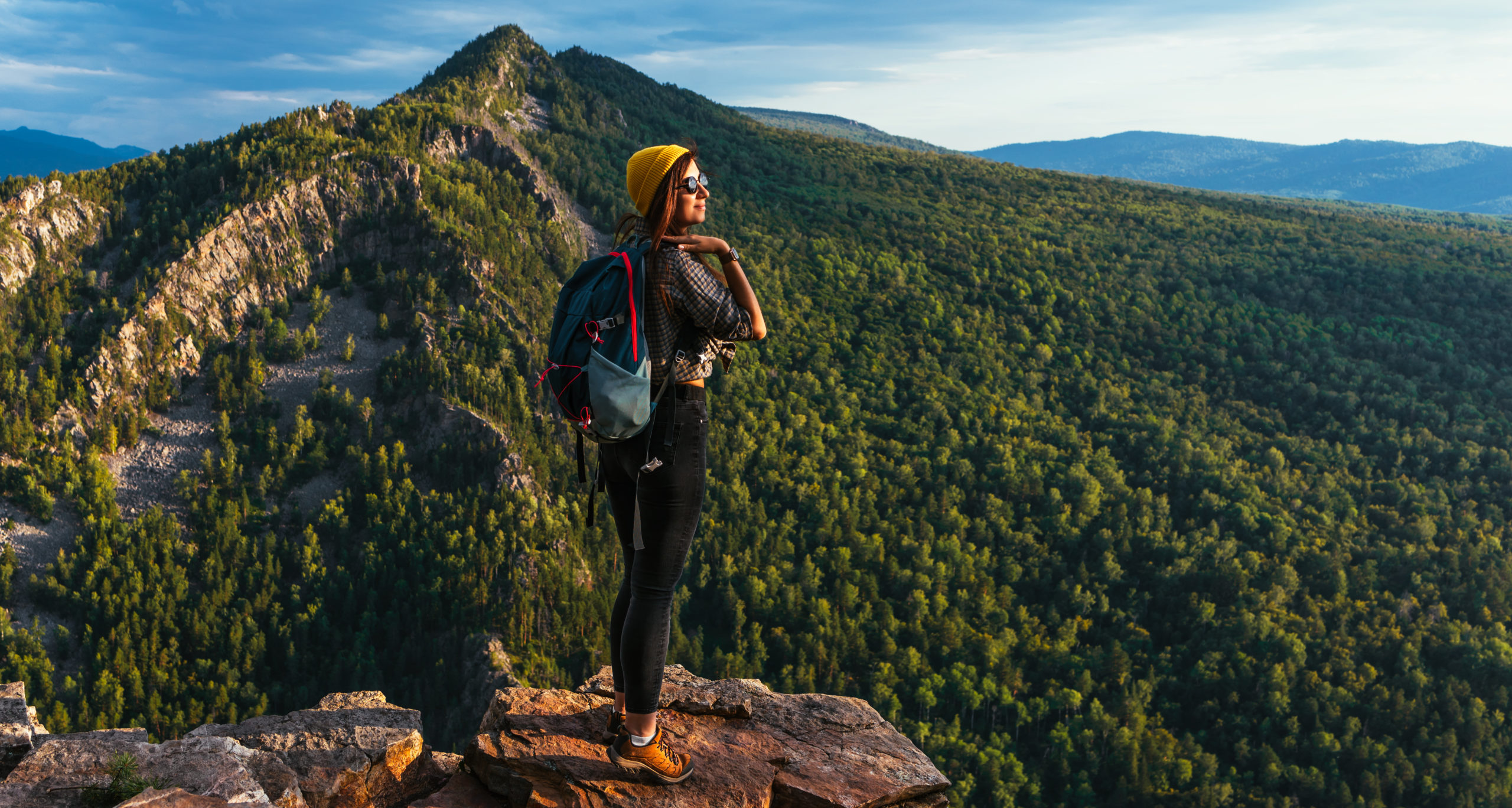 Adventure, travel and hiking concept. A tourist with a backpack and sunglasses on the background of mountains. A traveler meets the sunset in the mountains. Hiking in the mountains. Copy space